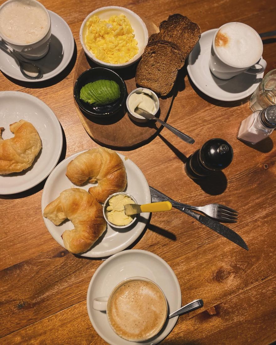Desayuno en la mesa: café con leche, medialunas, tostadas, palta y huevos revueltos