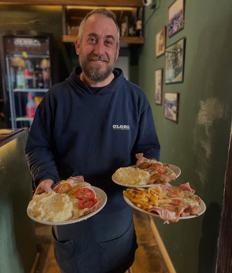 Mozo con tres platos de la casa: puré, revuelto y papas fritas