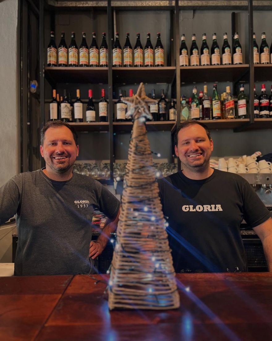 Los dueños detrás de la barra, con las botellas de vino de fondo